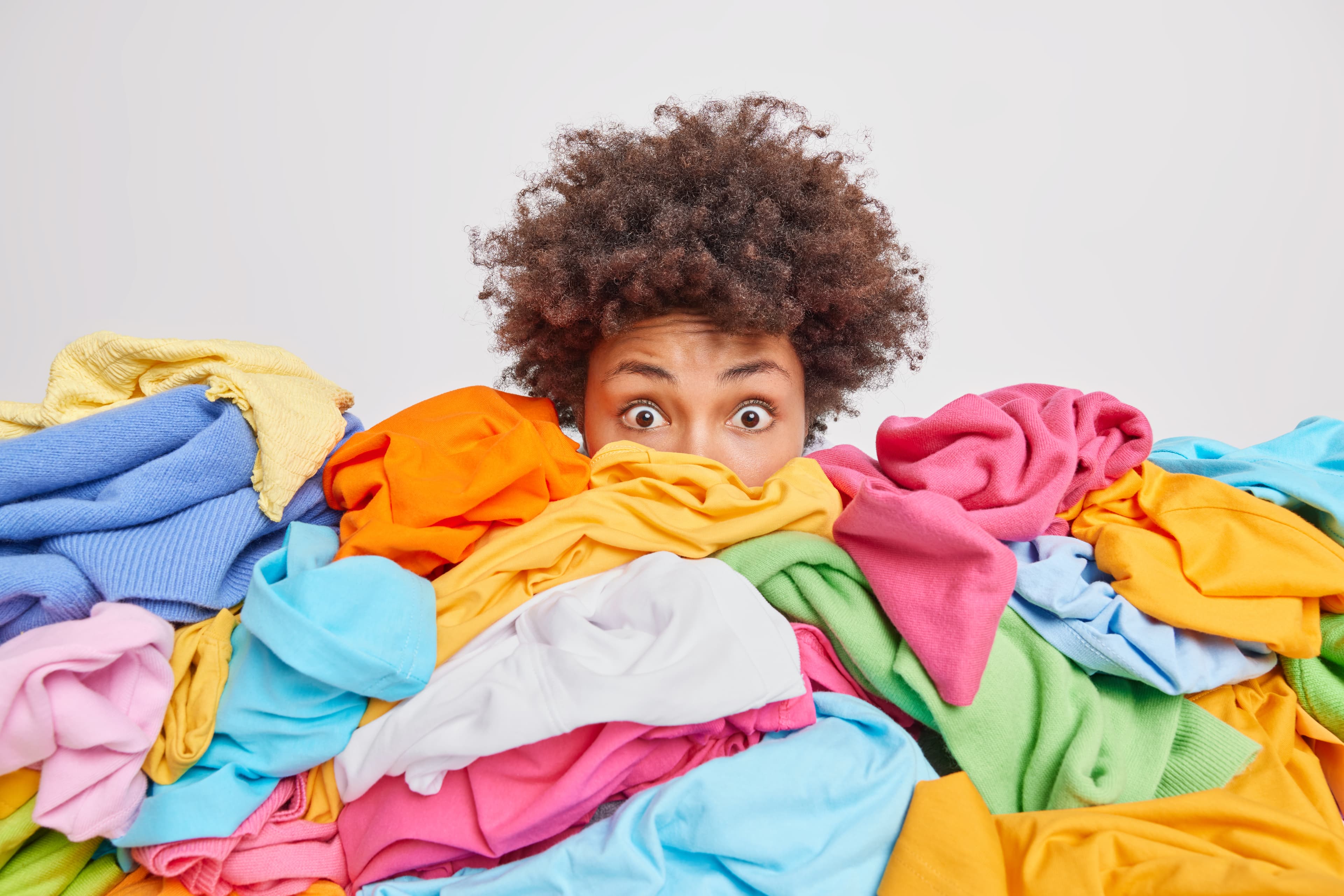 A woman peeking over a large pile of colorful laundry.